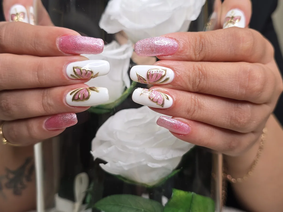 Ensemble d'ongles à motif papillon tenu près d'une rose blanche au salon Para Ella, Dubaï