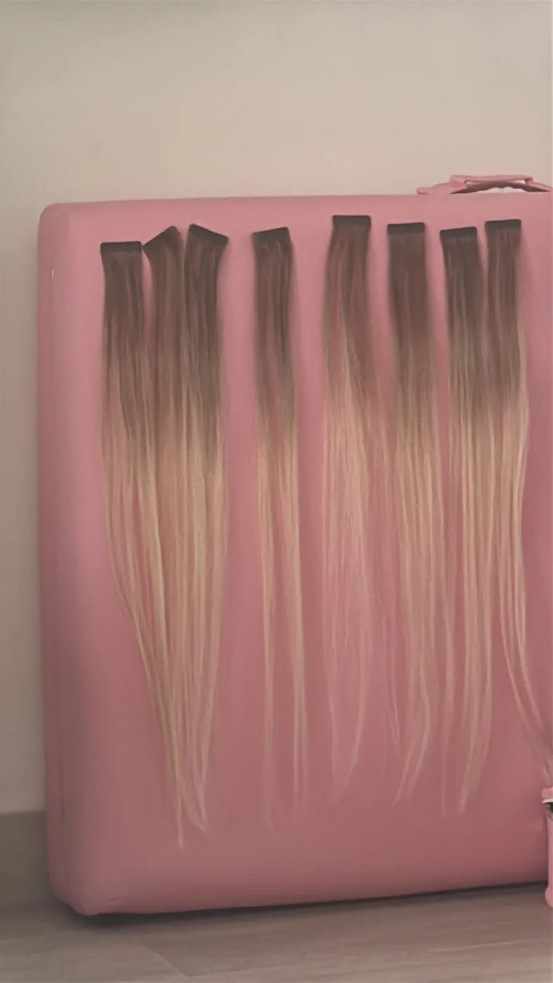 Ombre brown-to-blonde hair extension wefts hanging over a pink padded board
