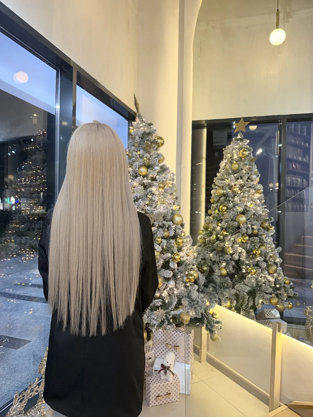 Back view of very long straight platinum blonde hair beside decorated gold Christmas trees