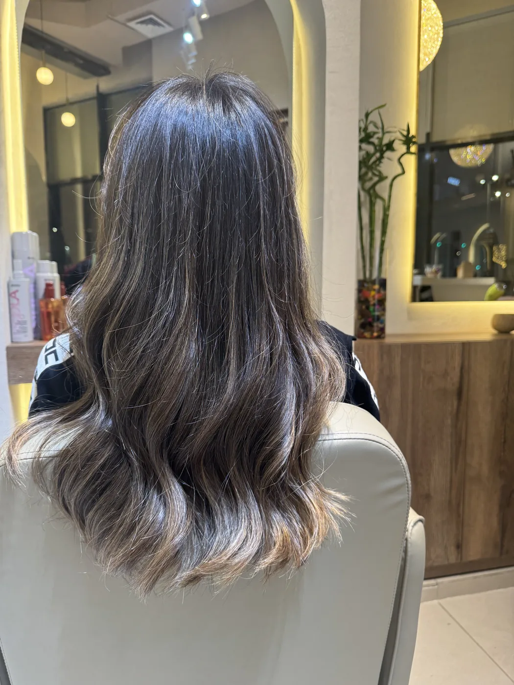 Back view of long wavy brown hair with balayage highlights in a salon chair