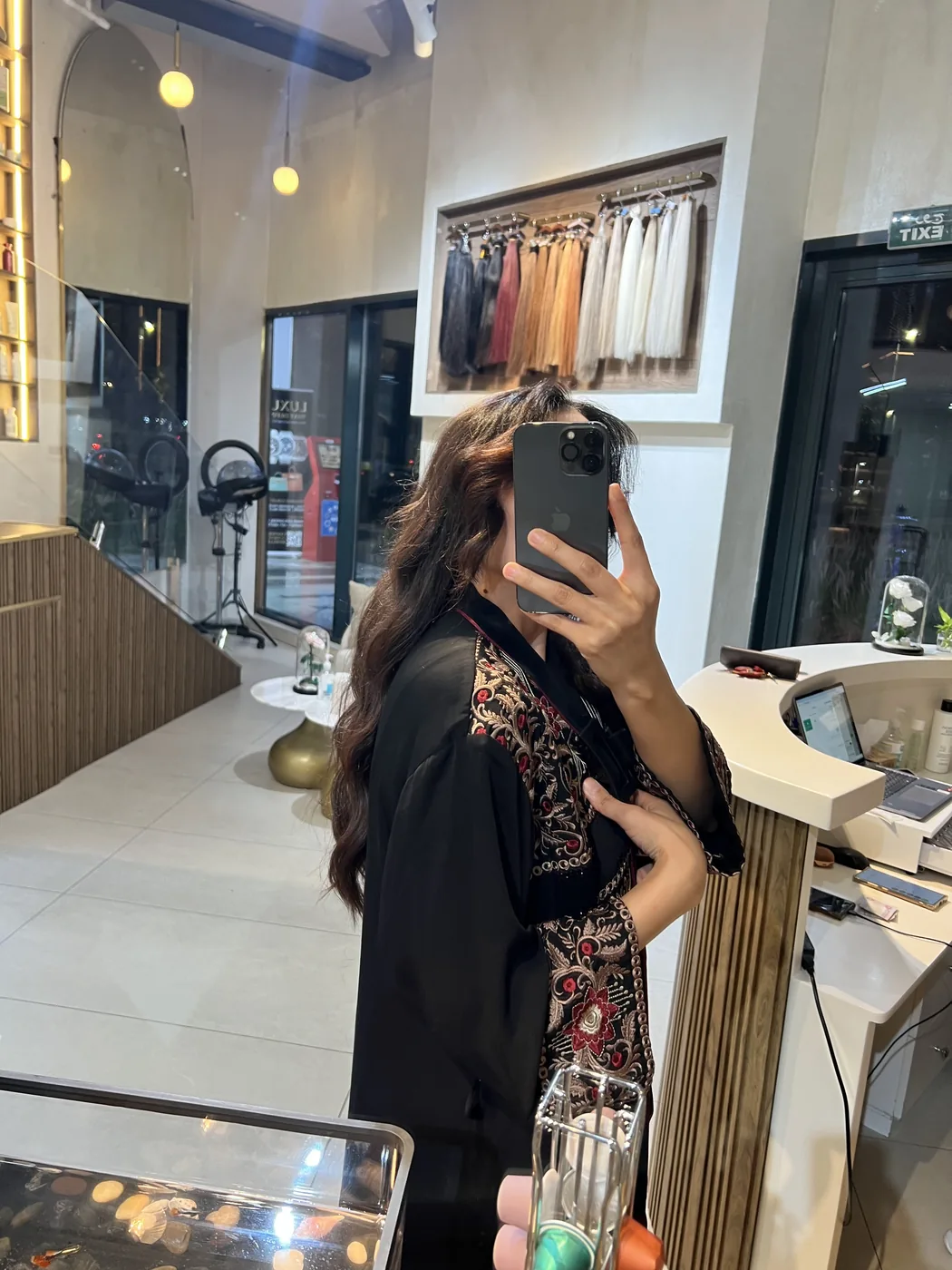 Woman in black embroidered abaya takes a mirror selfie inside the salon