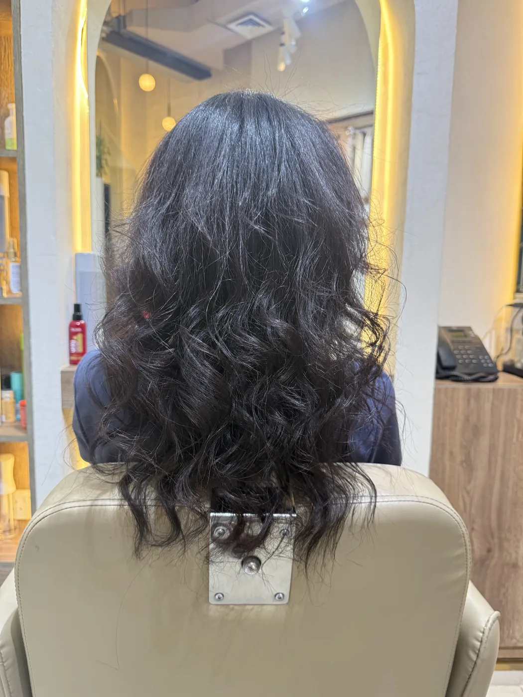 Back view of long dark wavy hair on a client in a salon chair