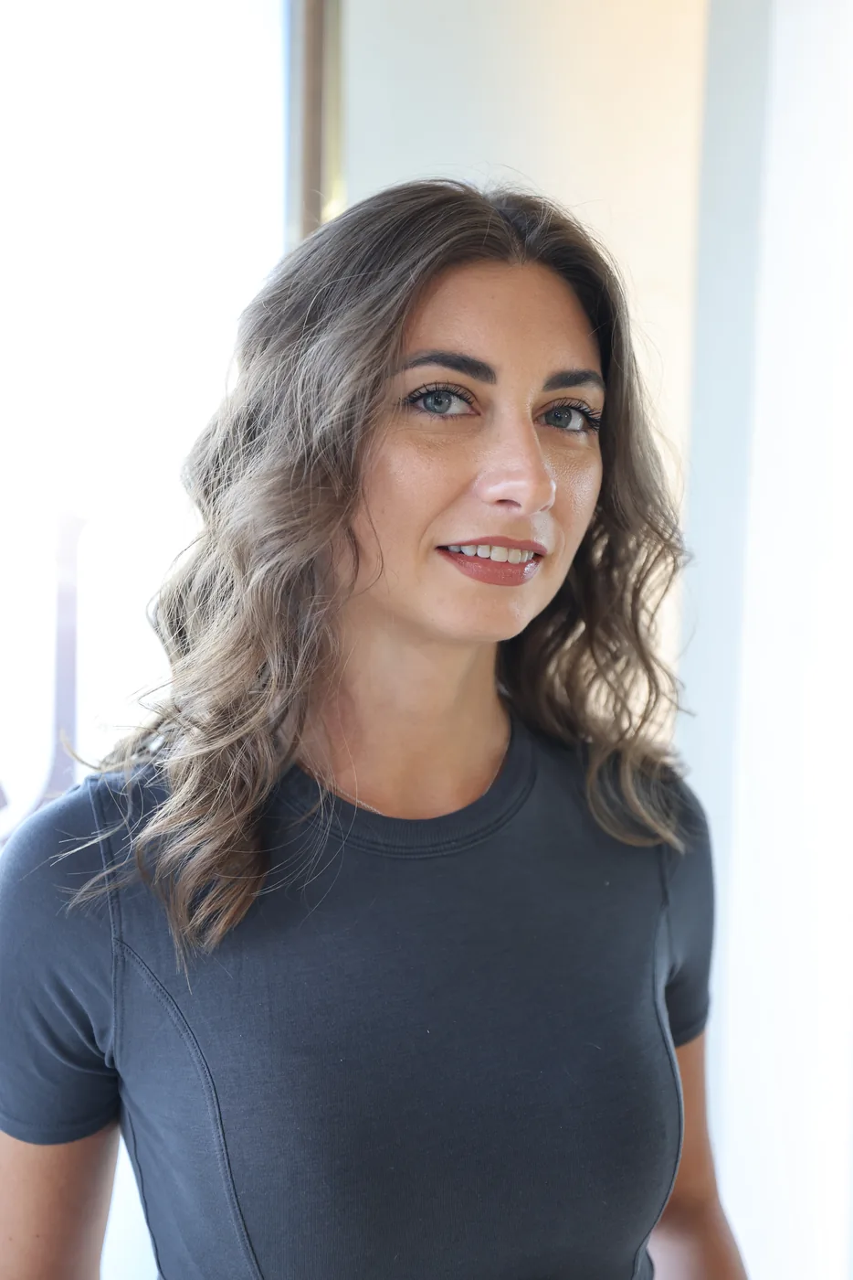 Woman with long wavy balayage hair standing beside a bright window