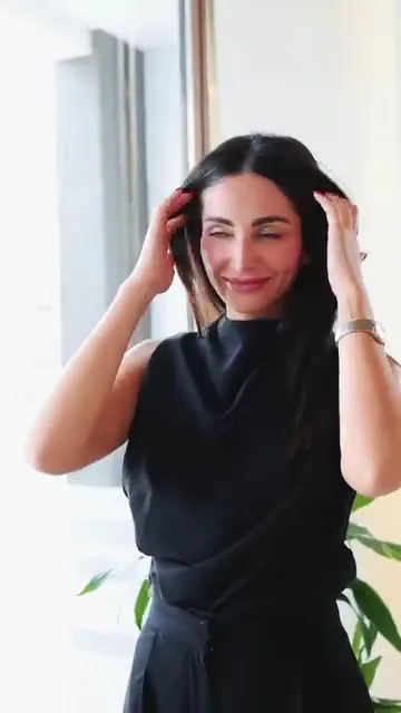 Smiling woman with long dark hair running both hands through it indoors