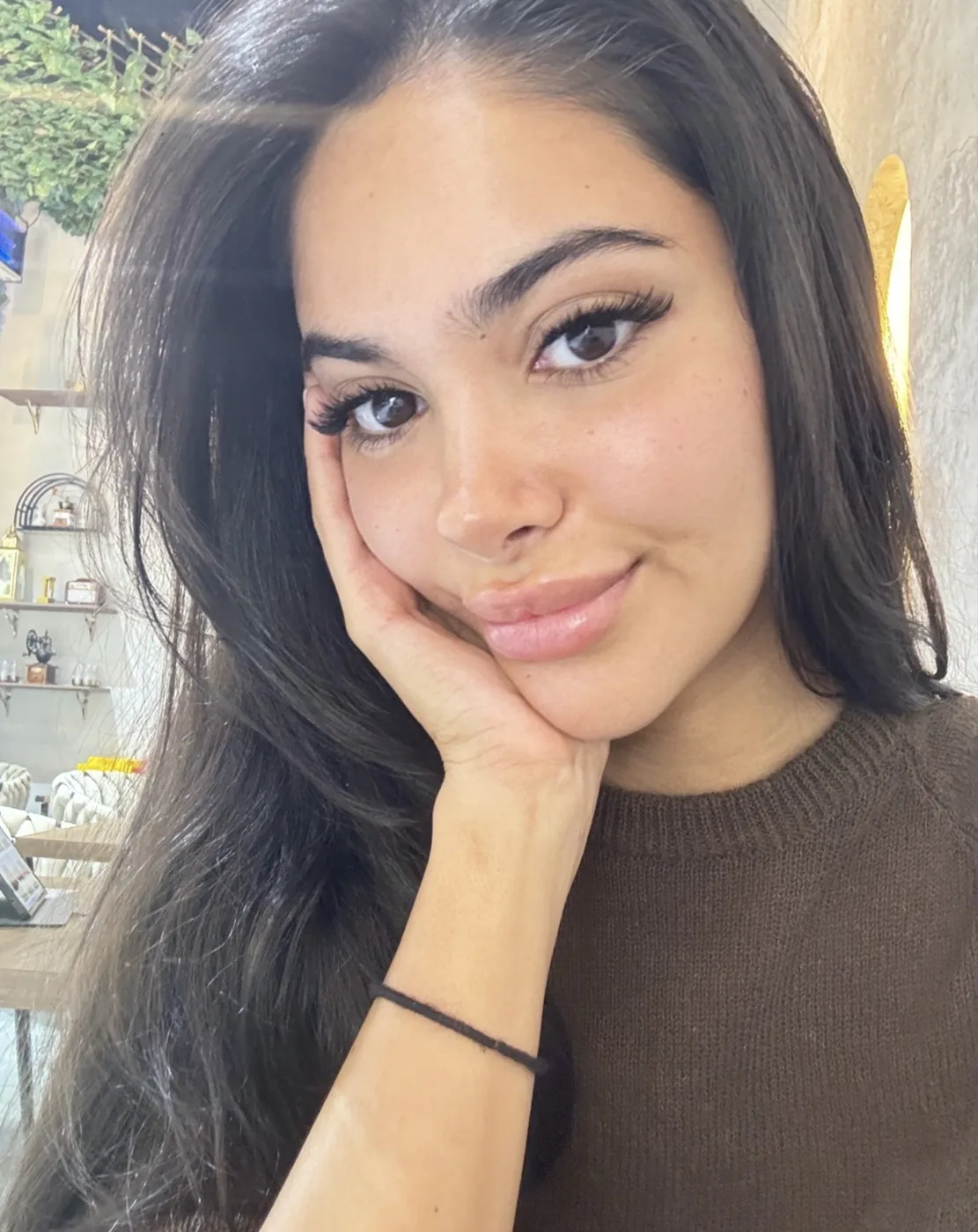 Young woman rests her cheek on her hand, long dark hair, defined brows and lashes