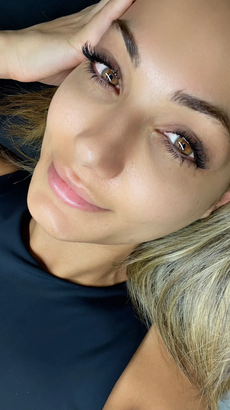 Close-up of a woman's face showing long lash extensions and defined dark eyebrows