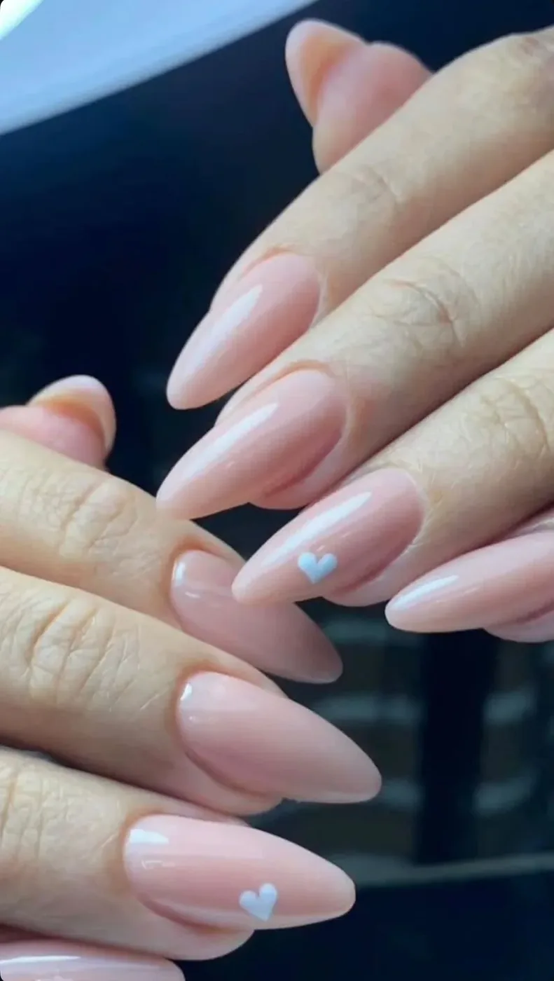 Close-up of almond-shaped nude pink nails with small pale blue heart details