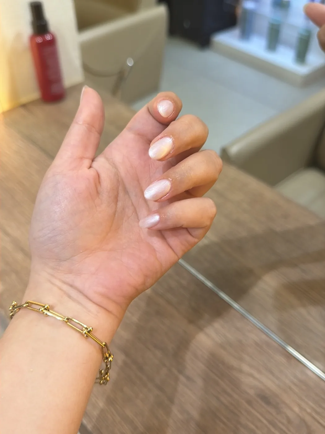 Hand with pale pearly oval manicure and gold chain bracelet in a salon