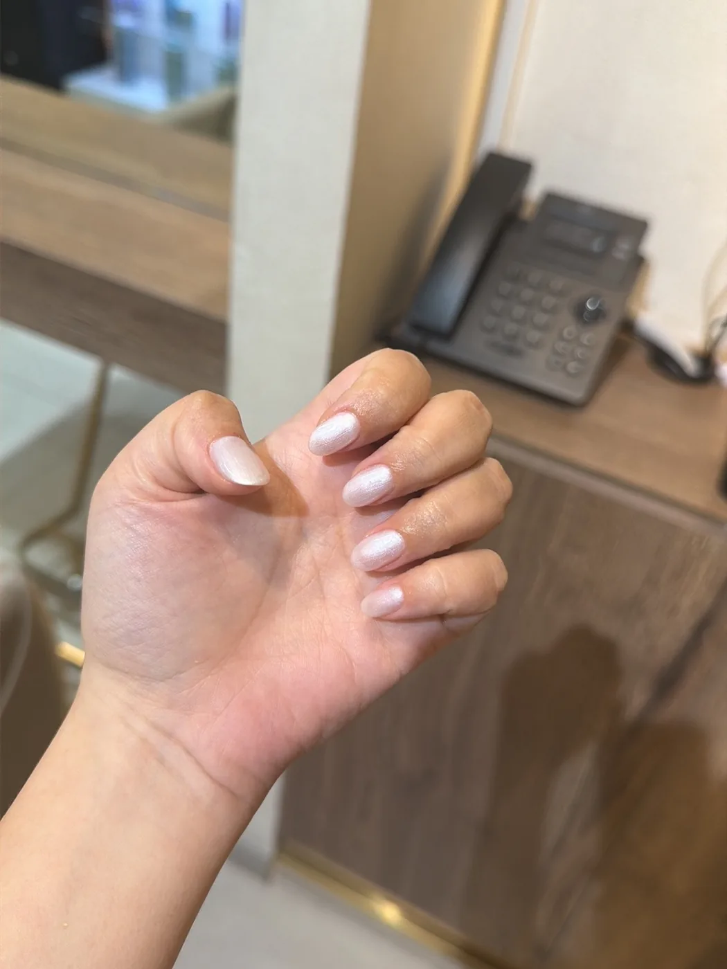 Hand with short pearly white nails held up at a salon reception desk