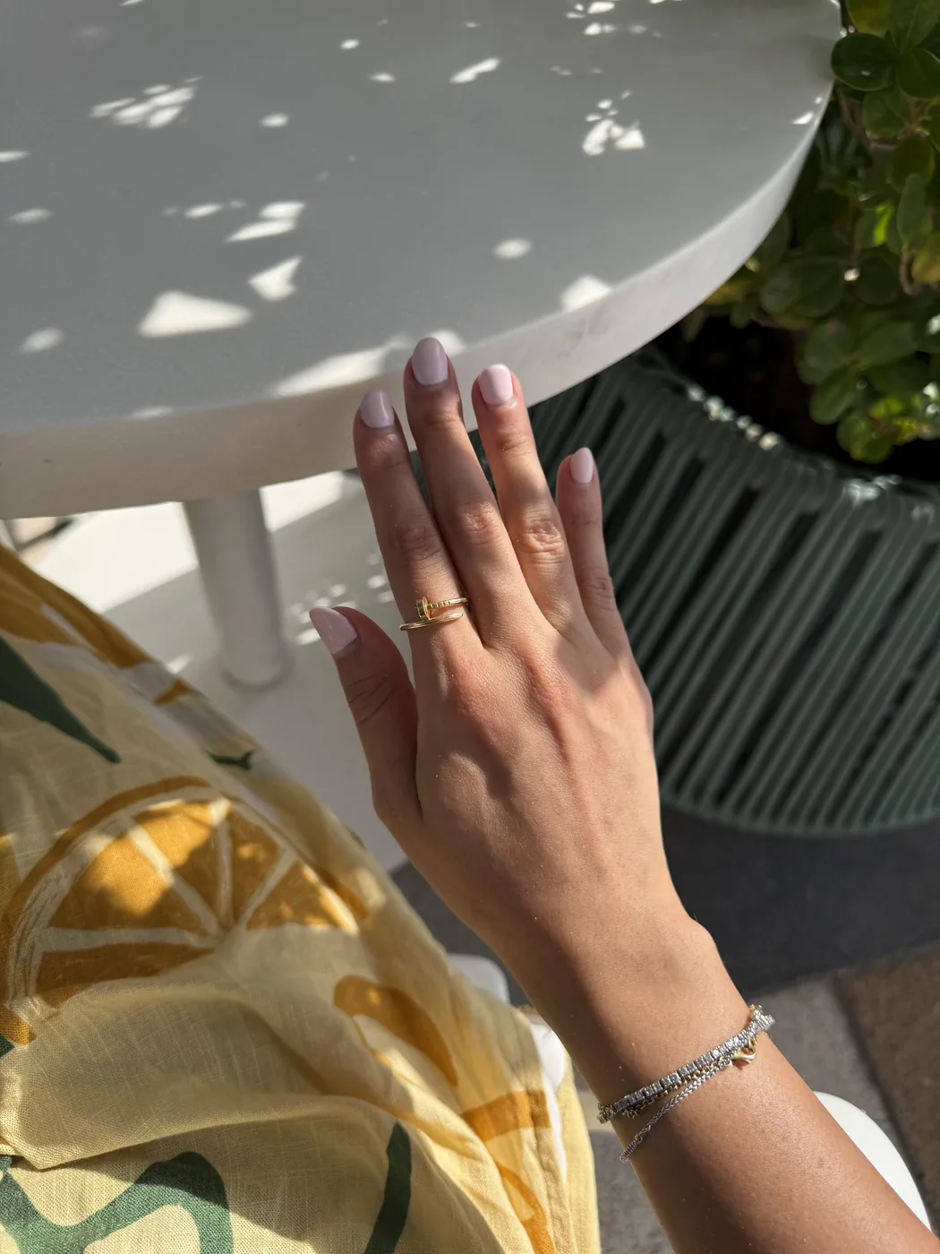 Hand with glossy pale pink nails resting on a white table in bright sunlight