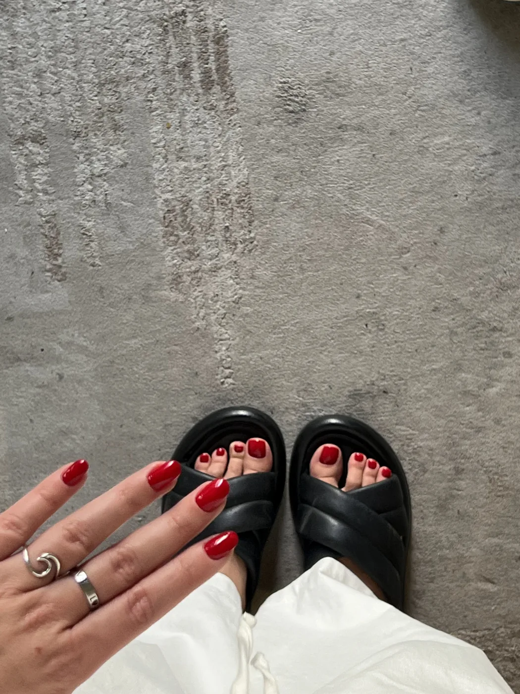 Overhead shot of a red manicured hand and red pedicure in black slide sandals