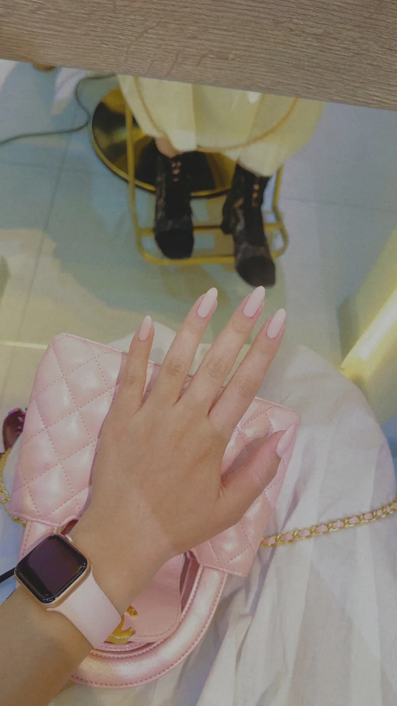 Hand with long pale pink nails resting on a quilted pink handbag