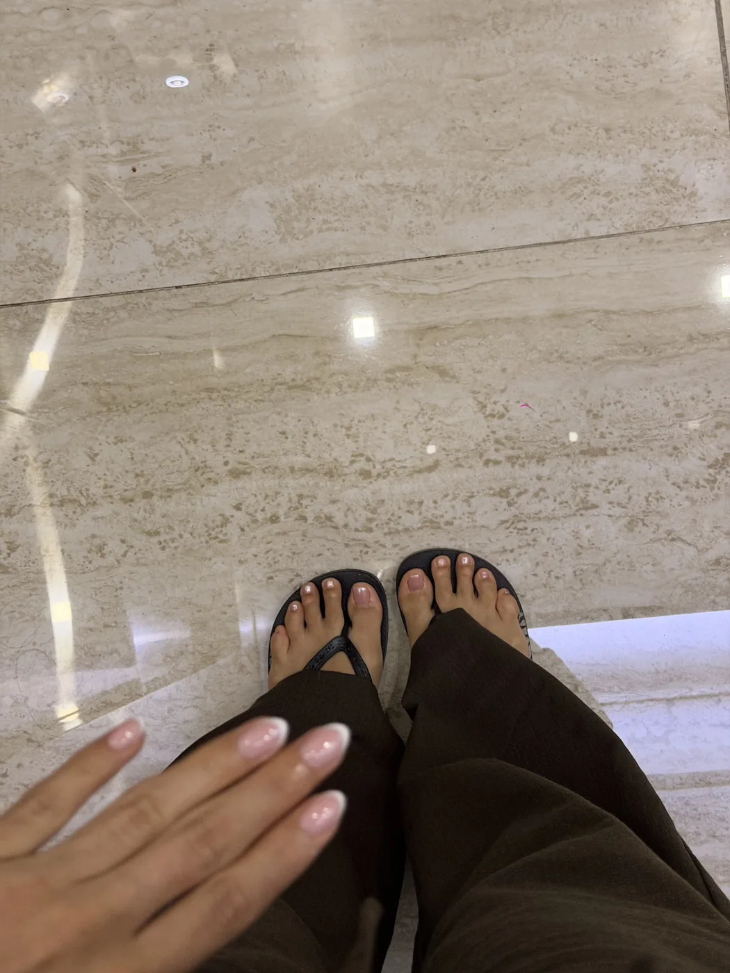Downward view of feet in black toe-separator slippers with painted toenails on marble floor