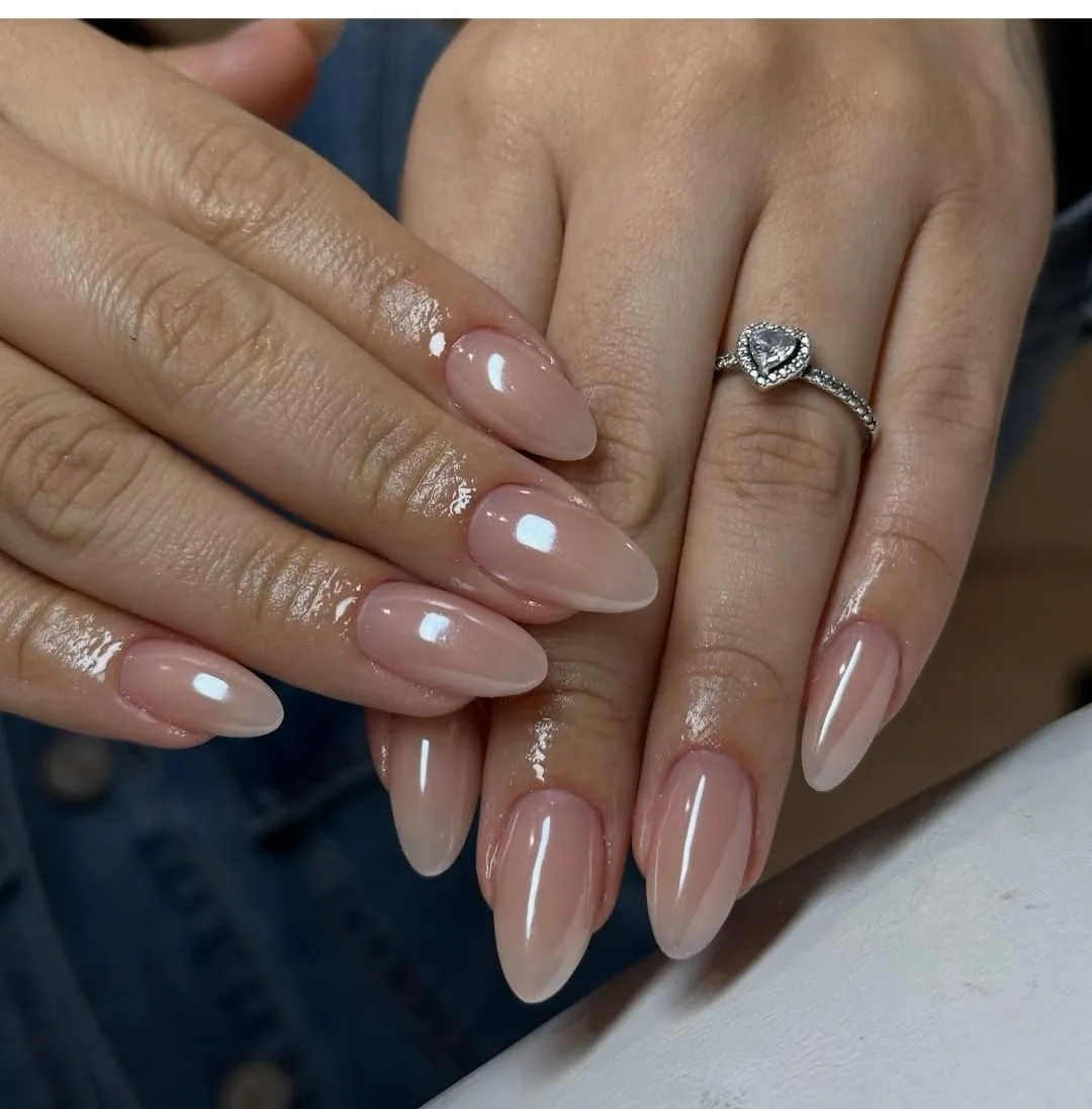 Two hands with long glossy nude almond nails and a heart-shaped stone ring