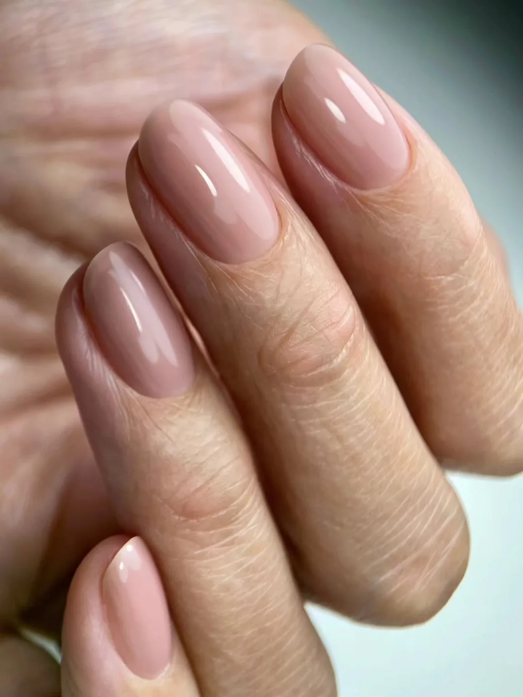Close-up of a hand with rounded nails in glossy nude-pink polish