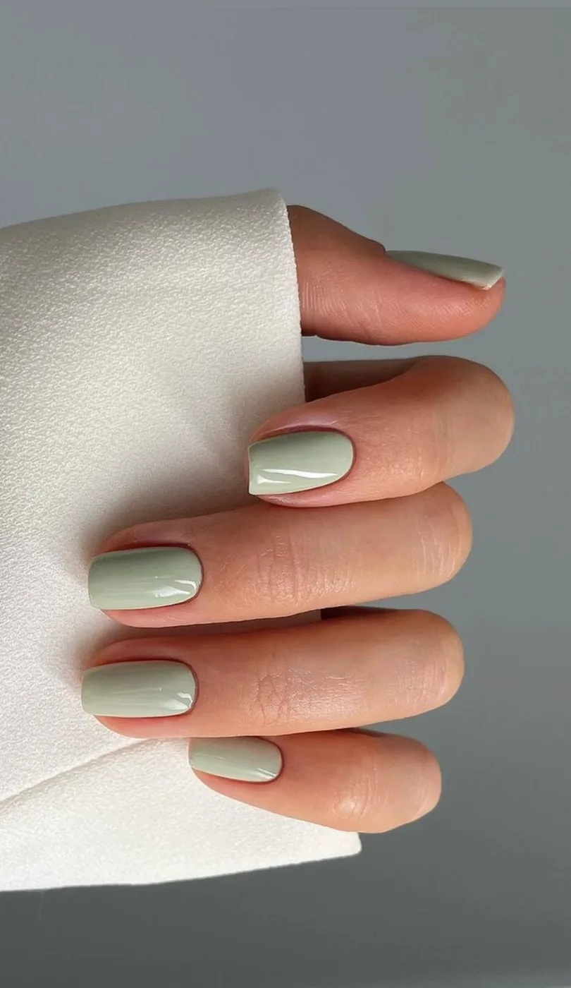 Hand with short square nails in sage green polish resting on towel