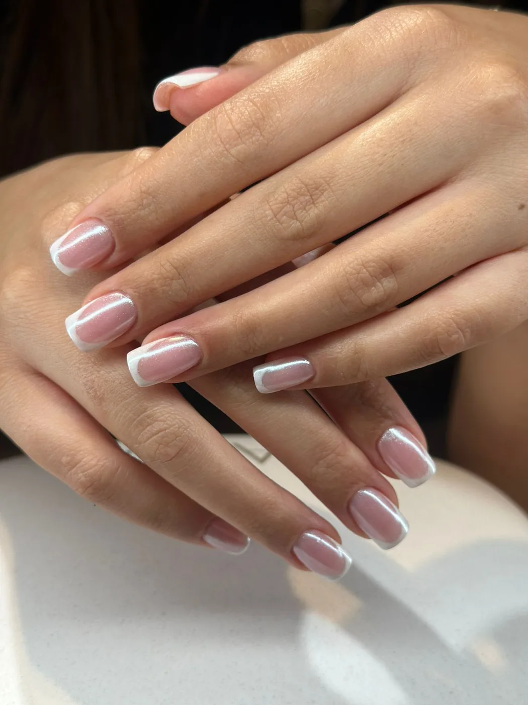 Close-up of two hands with a short square French manicure, pink base and white tips