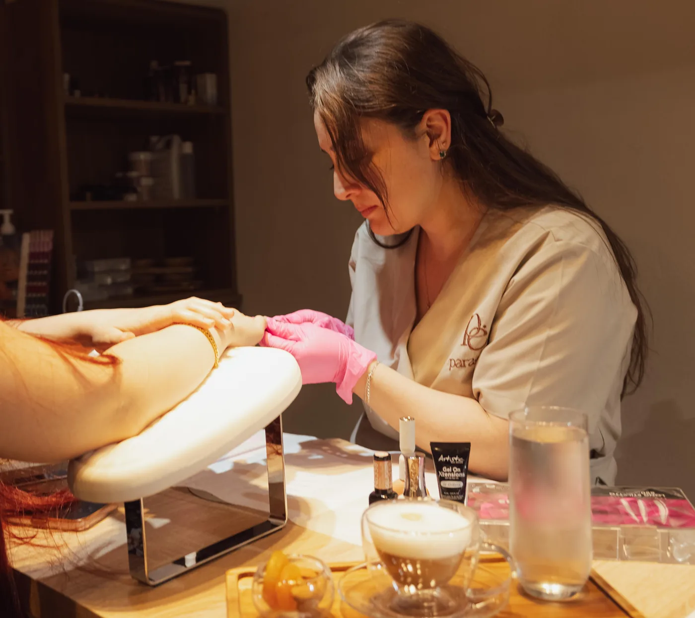 Nail technician in pink gloves works on a client's hand at a manicure table
