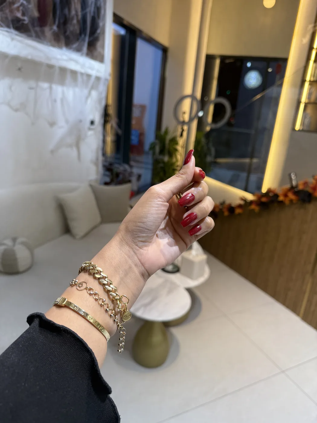 Hand with long dark red nails and gold bracelets raised in a salon lounge