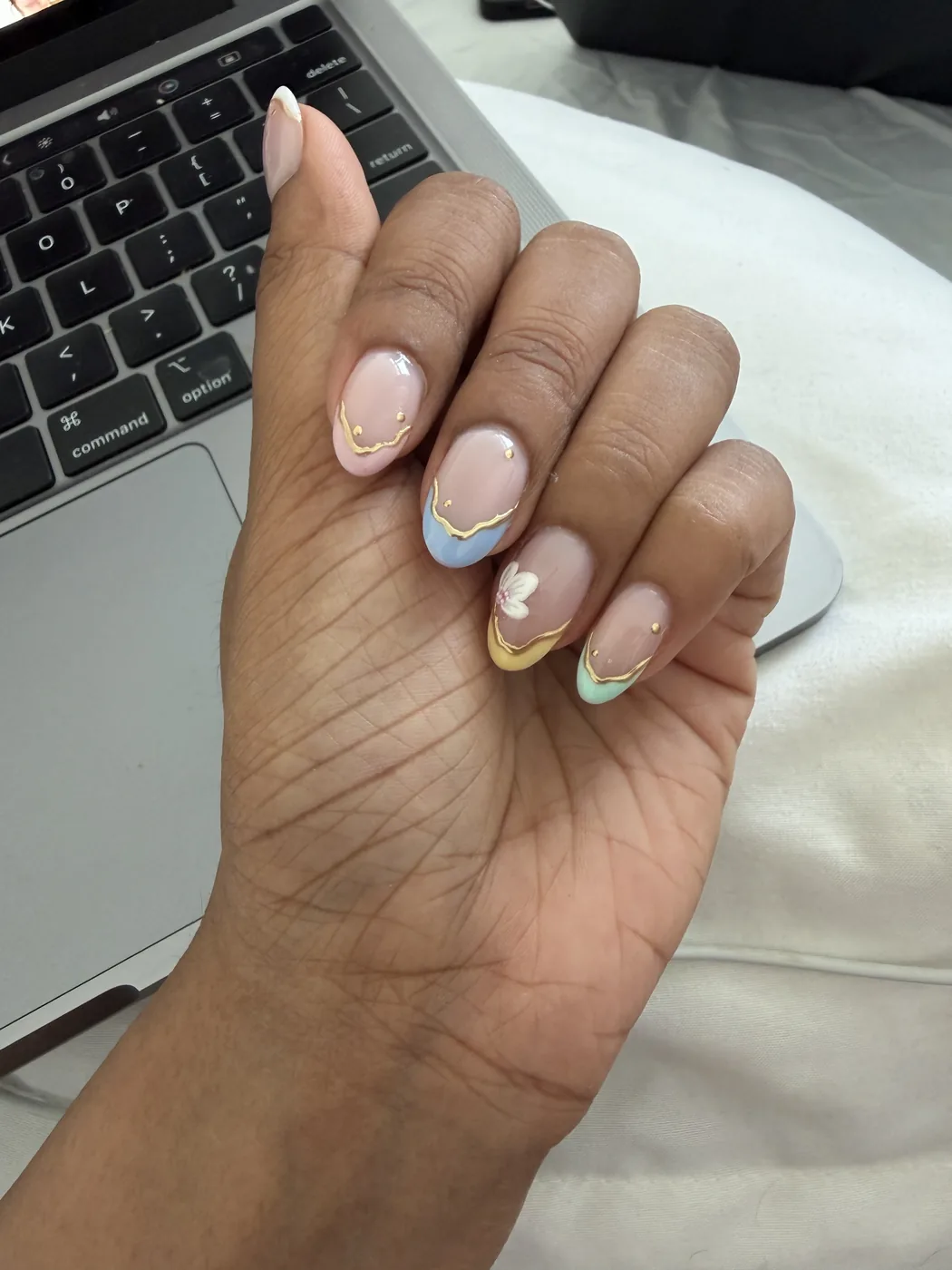 Hand with almond nails in pastel blue, yellow and mint French tips