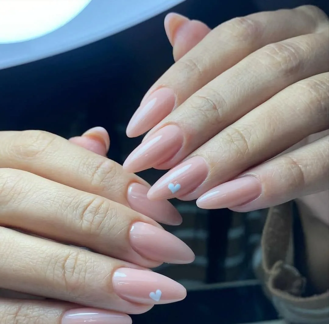 Two hands with almond nude-pink gel nails and small pale blue hearts