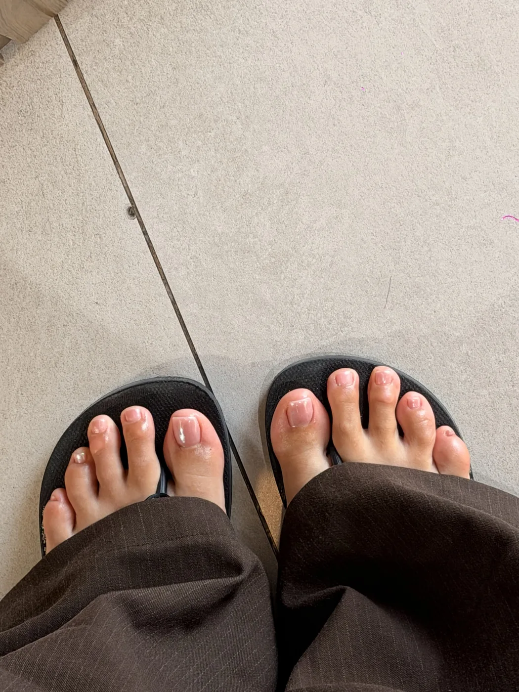 Overhead view of feet in black salon slippers with pale French pedicure
