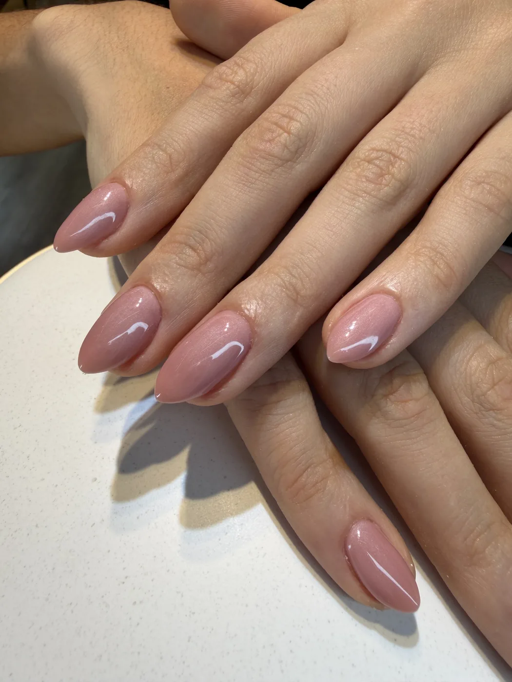 Close-up of two hands with glossy nude-pink almond-shaped gel nails