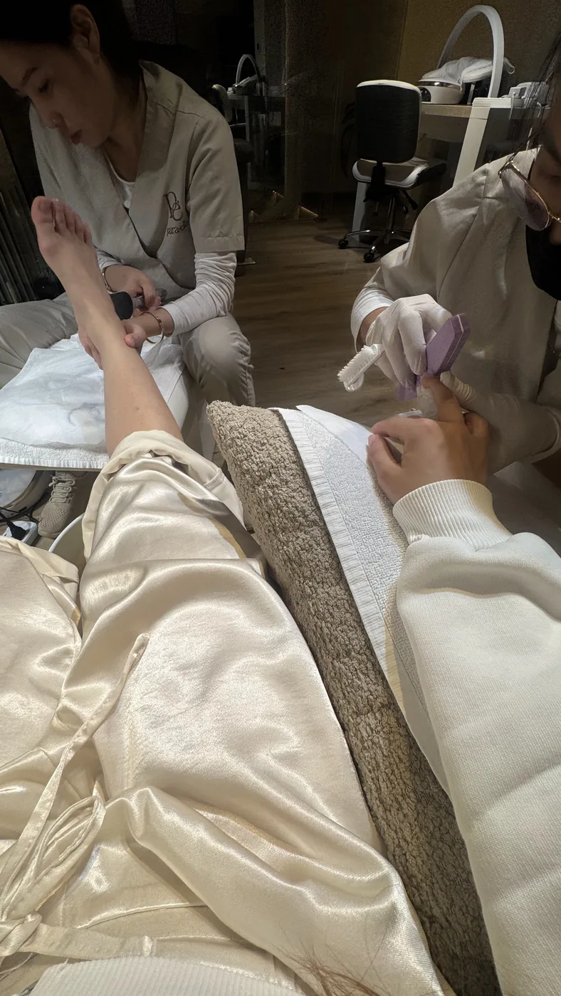 Client reclined while one therapist works on her raised foot and another on her face
