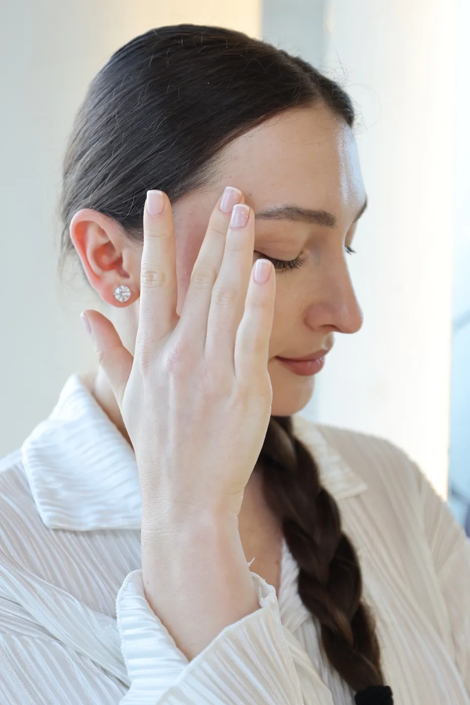 Woman with braided dark hair, eyes closed, hand raised showing pale manicured nails