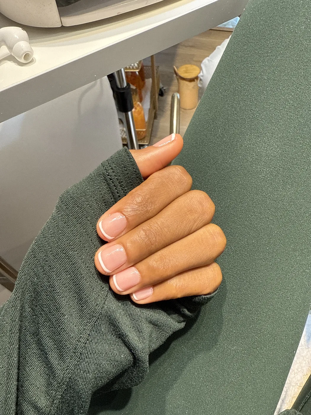 Hand with short French manicure resting on green fabric in a salon