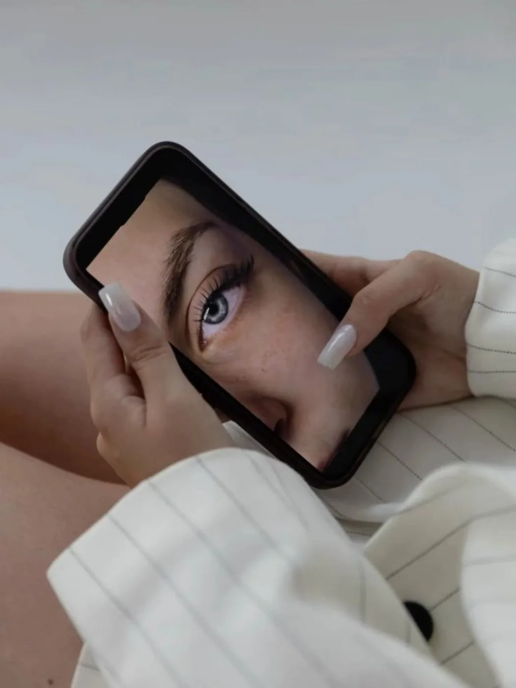 Hands with long nude square nails holding a phone showing a close-up eye