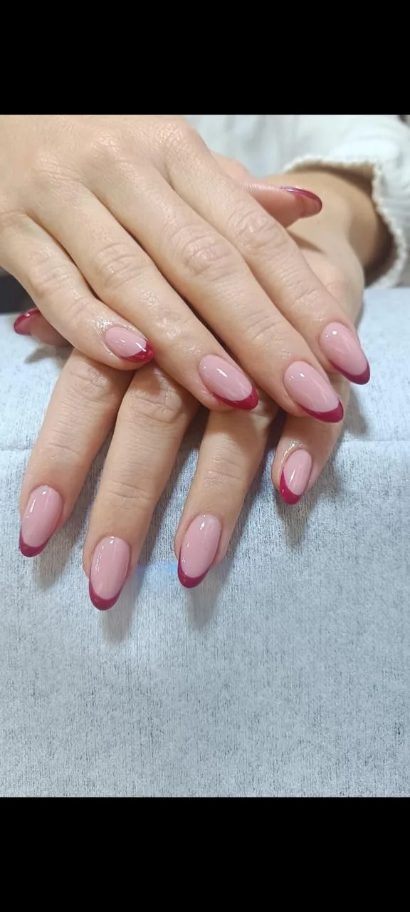 Two hands with almond nails in nude pink with deep red French tips