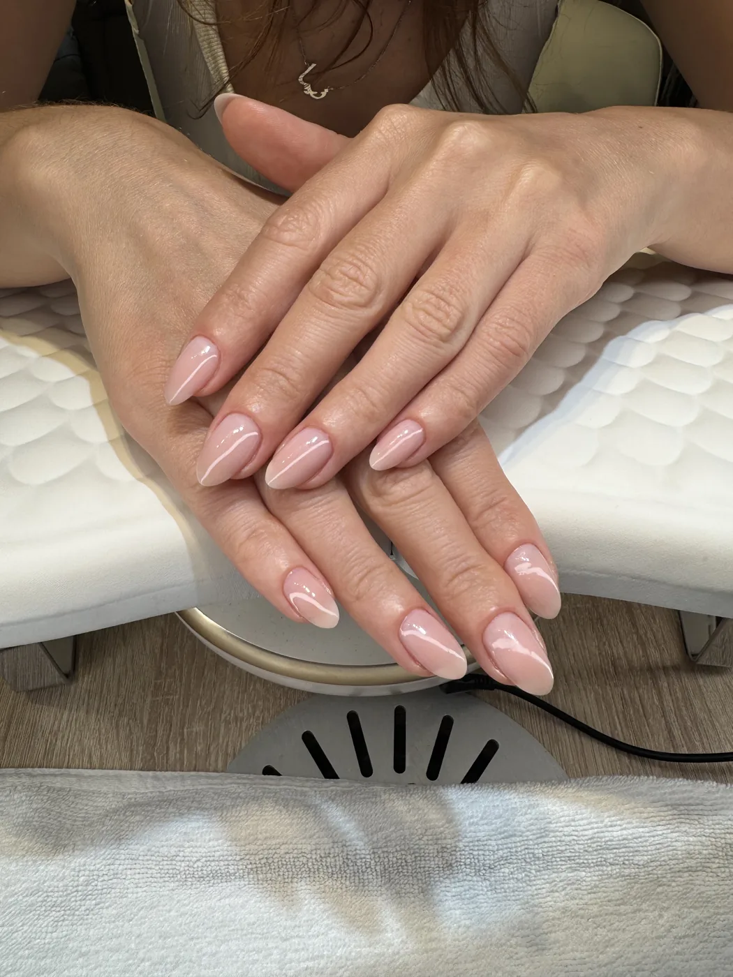 Two hands with long almond nails in glossy nude pink on manicure cushion