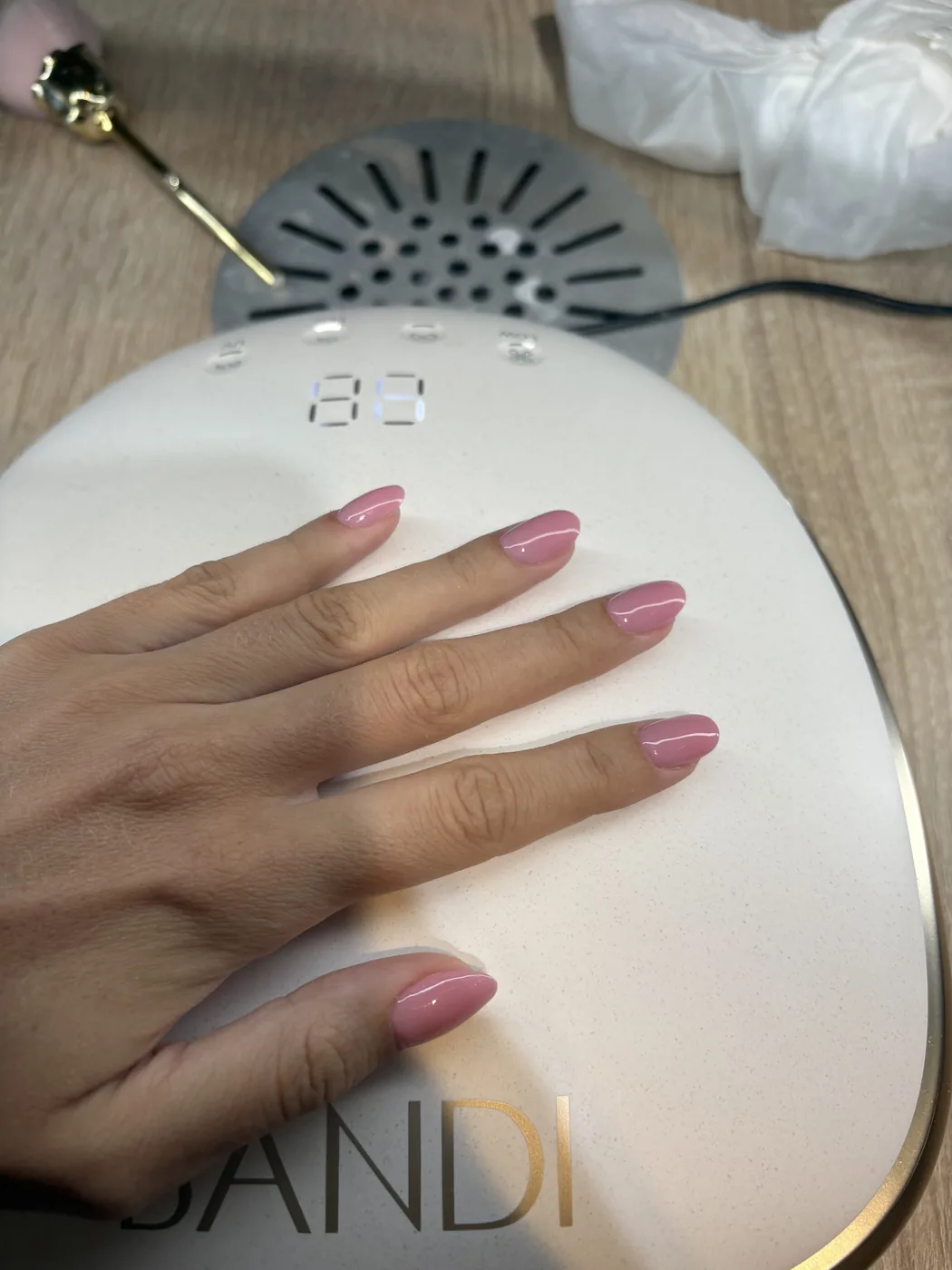 Hand with pink almond nails resting on a white UV nail lamp