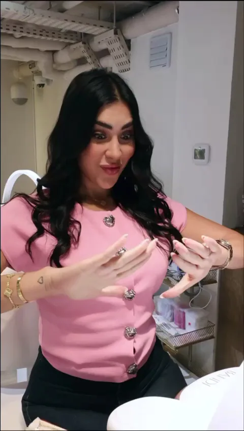 Woman in a pink top holding both hands up to show long nail extensions