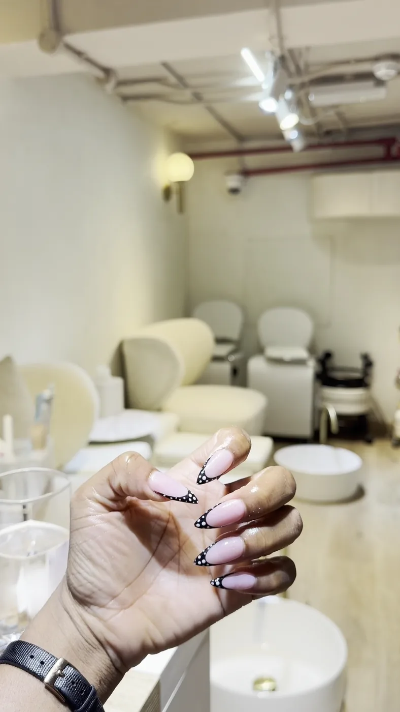 Hand with pink nails and black French tips held up in a pedicure area