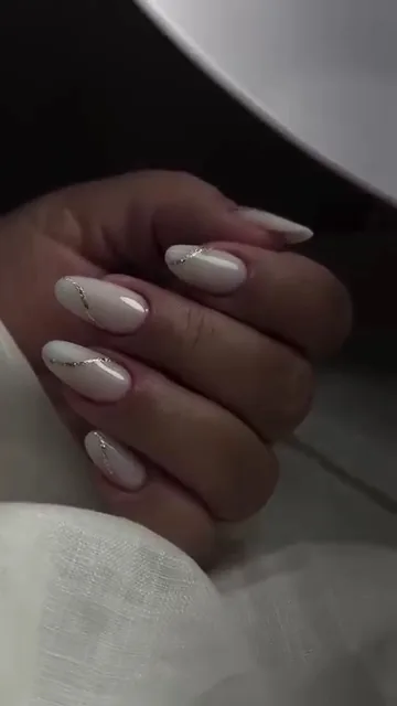 Close-up of a hand with almond-shaped milky white nails and thin silver line accents