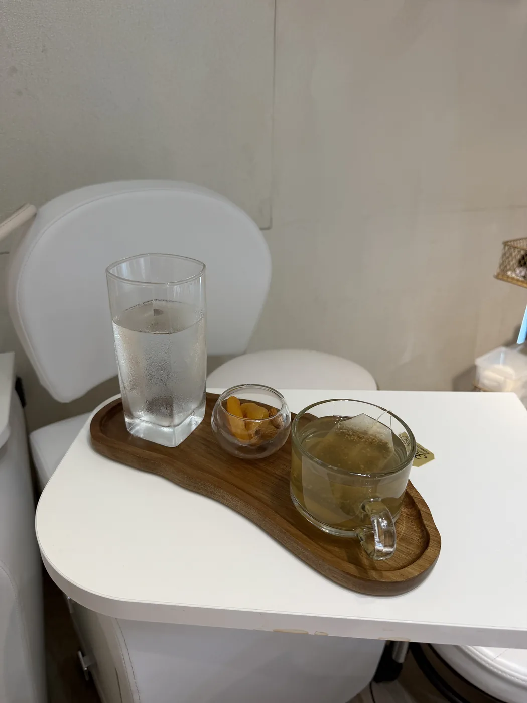 Wooden tray with water, tea and dried fruit on a white table by a white chair