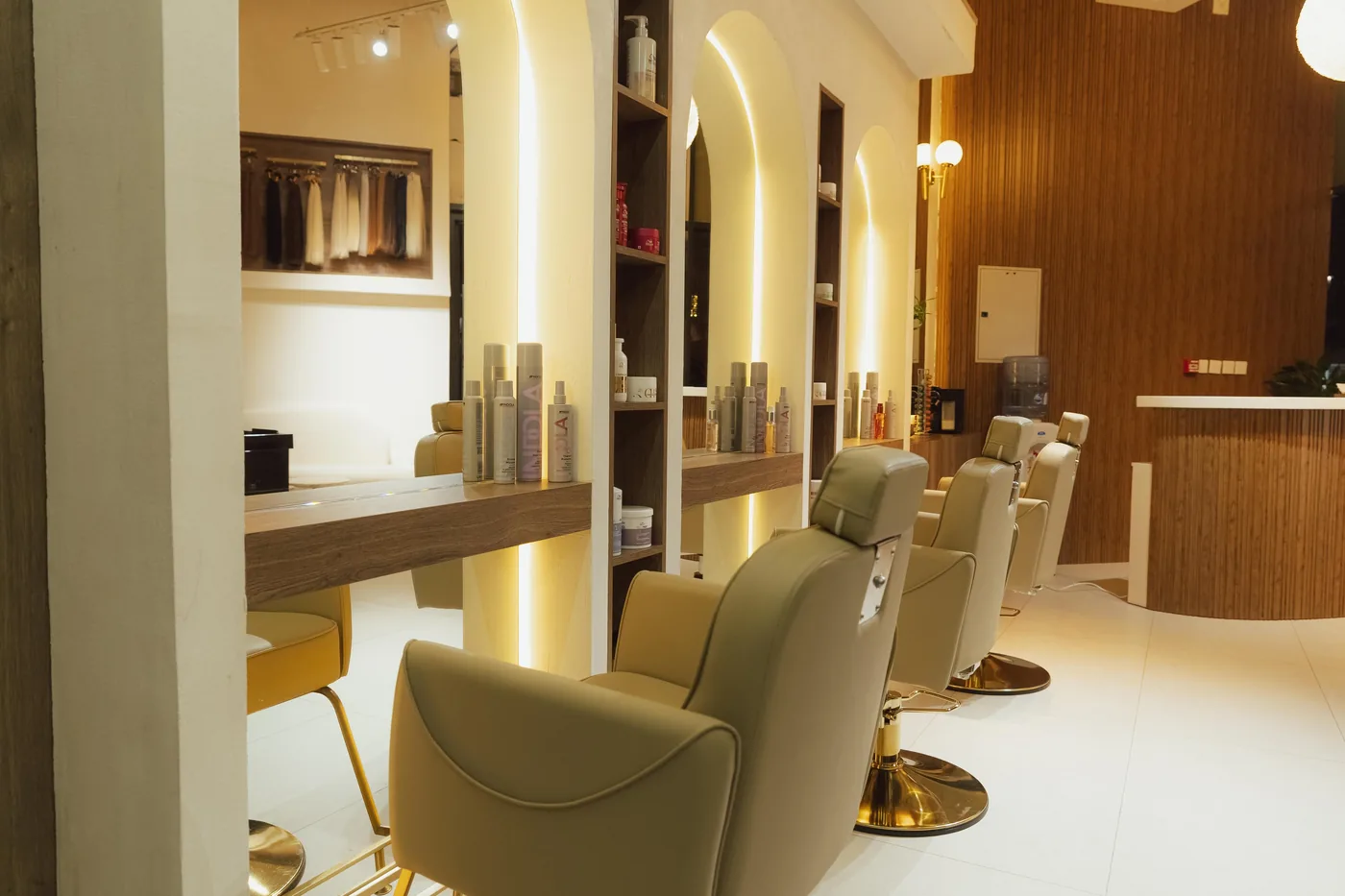 Row of cream styling chairs facing arched lit mirrors with product shelves nearby