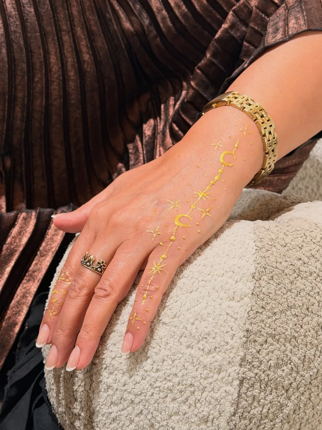 Hand with gold star and crescent designs on skin, gold bracelet, French-tip nails