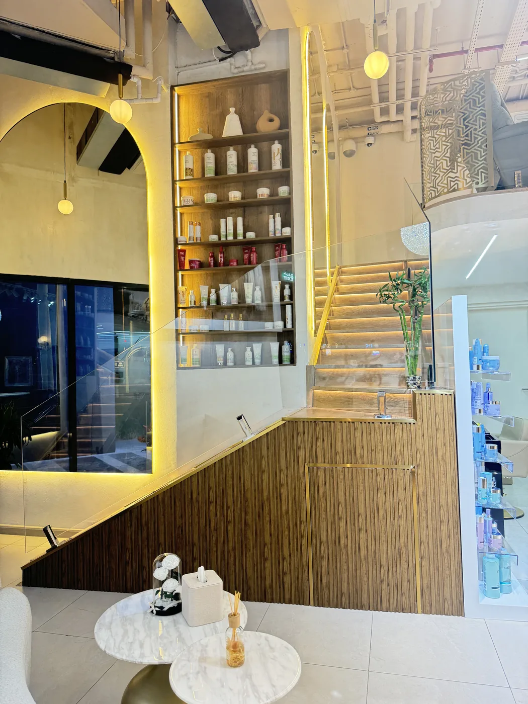 Salon staircase, product shelves and marble tables with flowers under glass dome