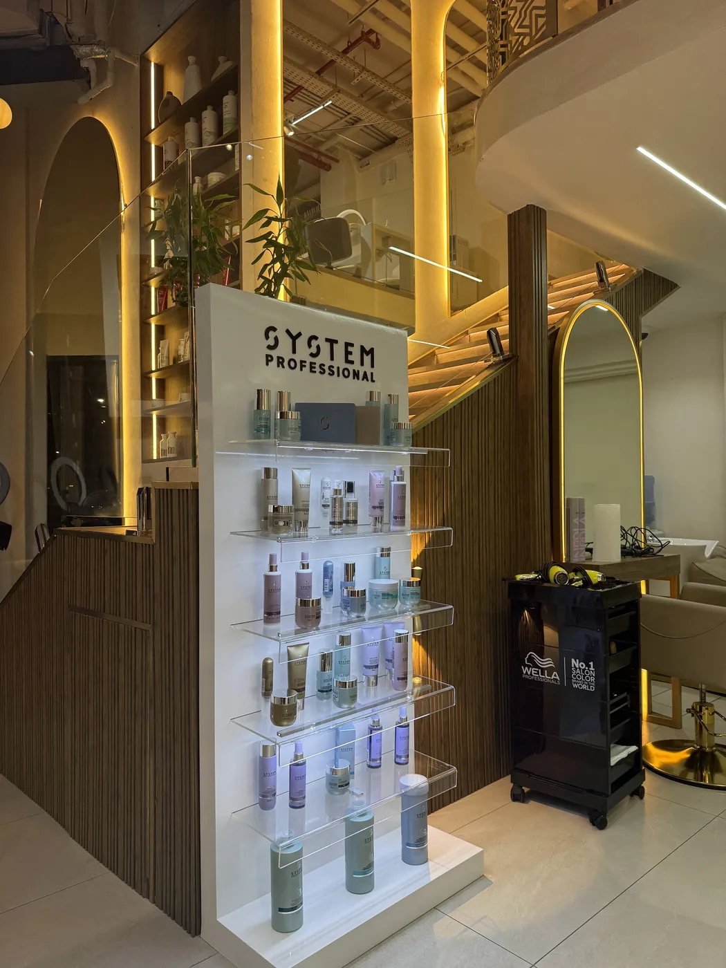 System Professional haircare display on acrylic shelves beside a black Wella trolley