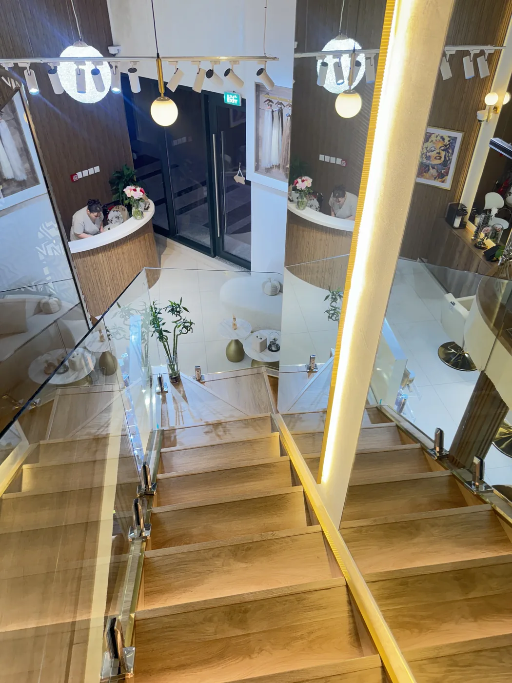Wooden staircase with a glass balustrade looking down onto the salon reception desk