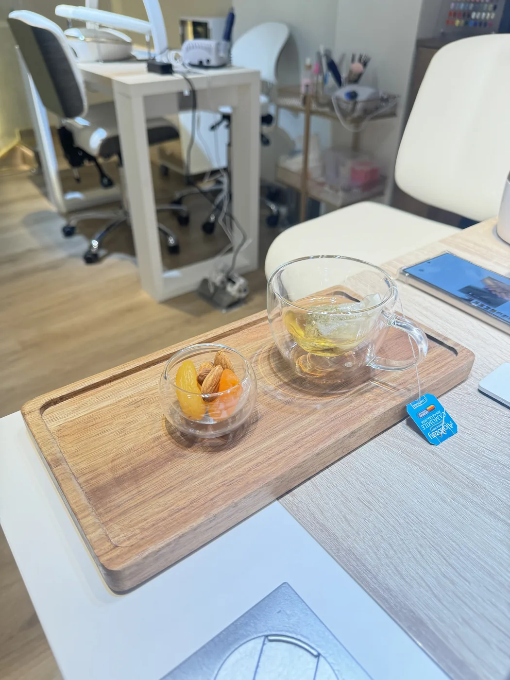 Wooden tray holding green tea and dried fruit beside an empty nail station