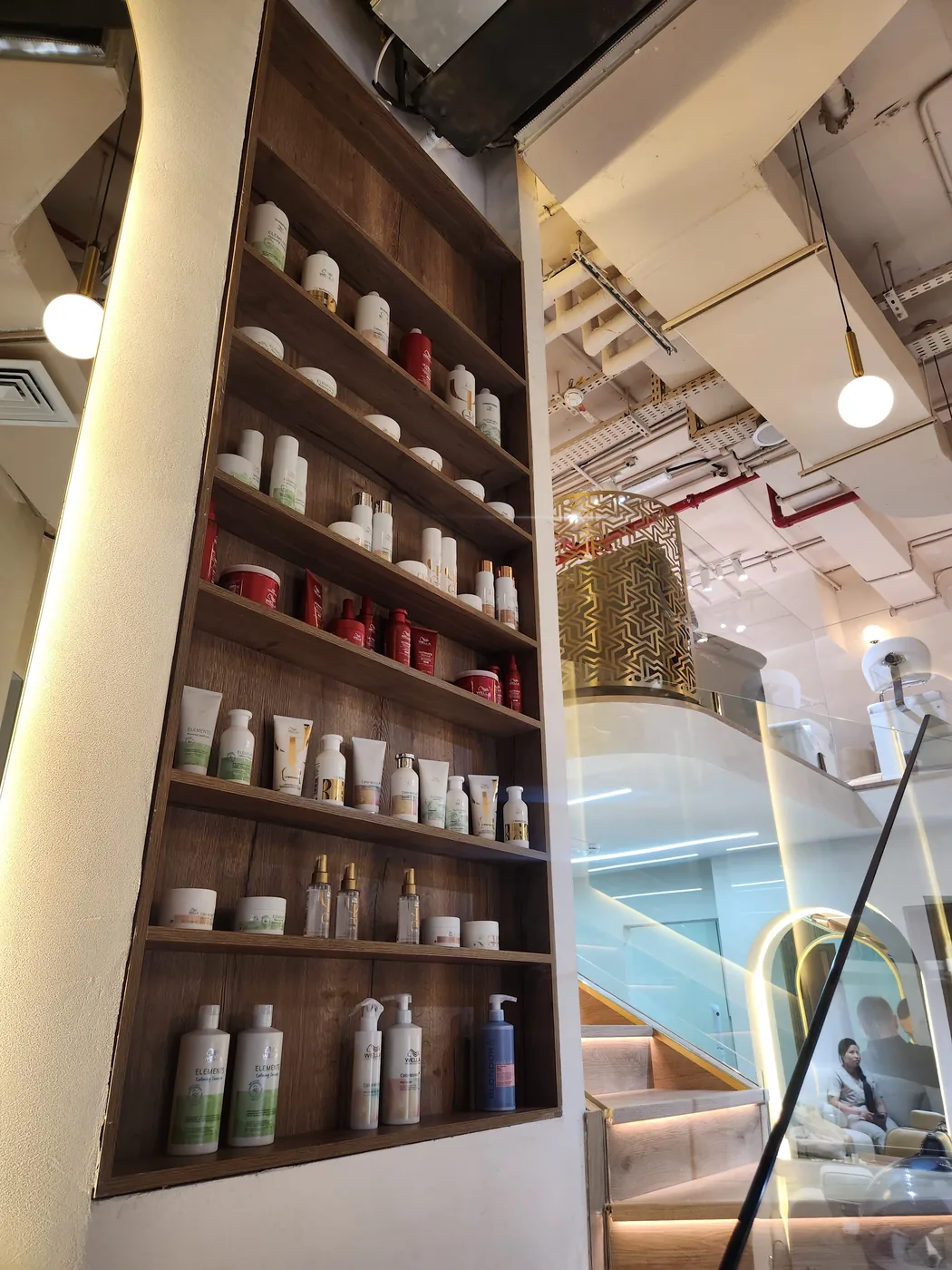 Wooden wall shelves stocked with haircare and skincare bottles beside a salon staircase