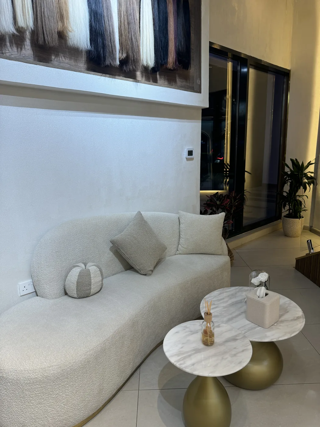 Curved cream boucle sofa with marble side tables under a hair-extension swatch display